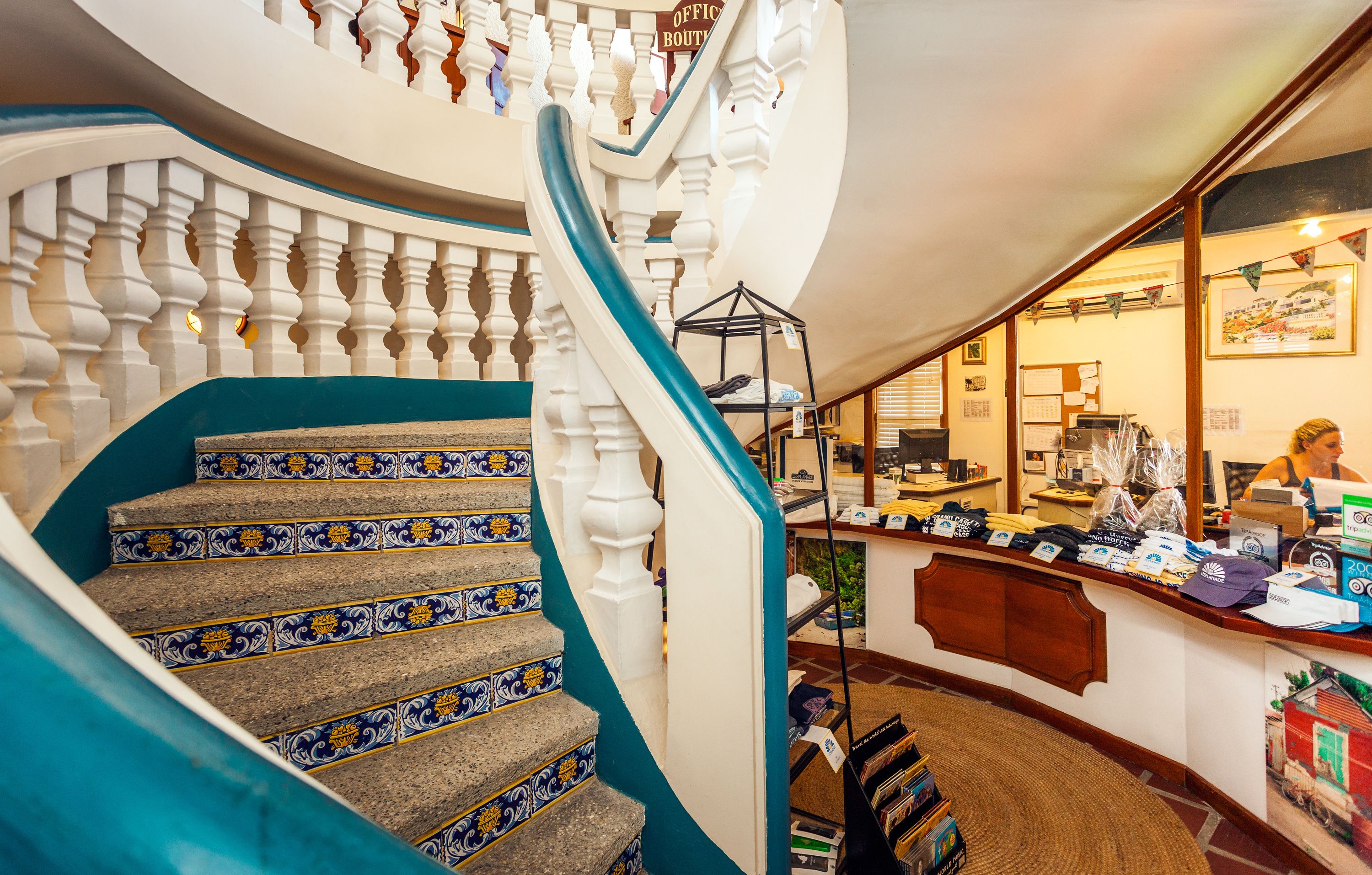 A grand staircase with ornate railings and patterned steps, leading to a reception area with a counter displaying merchandise and a framed picture on the wall.