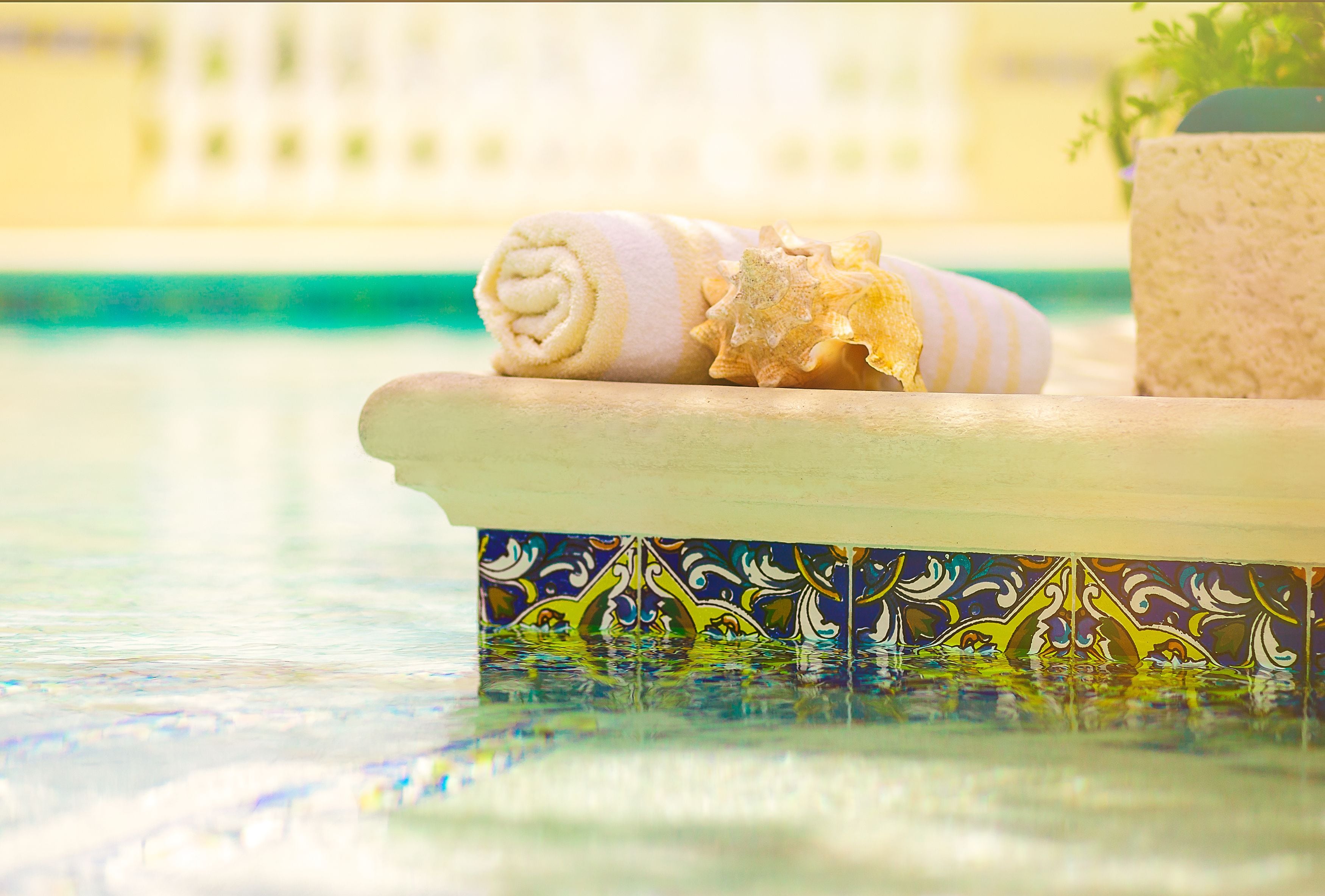 Un asciugamano e conchiglie su una superficie piastrellata vicino a una piscina.