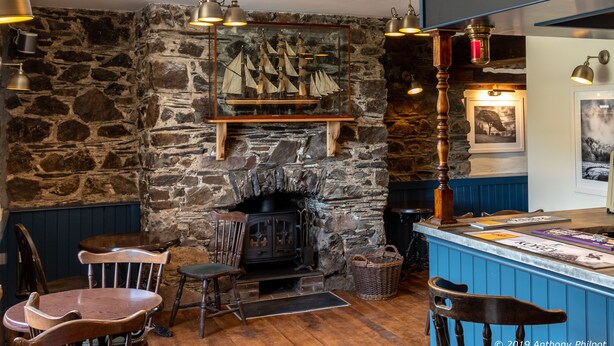 A cozy room with a stone wall, a fireplace, wooden furniture, and a bar area. - The Wilcove Inn (Torpoint)