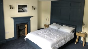 A bedroom with a large bed, a fireplace, and a nightstand with a lamp. - The Wilcove Inn (Torpoint)
