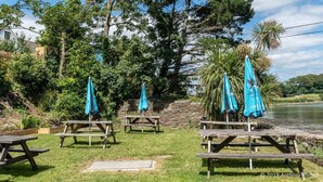A lakeside picnic area with wooden benches and blue umbrellas, surrounded by trees and a stone wall. - The Wilcove Inn (Torpoint)