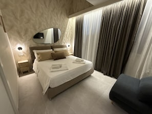 Un dormitorio moderno con una cama grande, una mesita de noche, un espejo y un sillón oscuro.