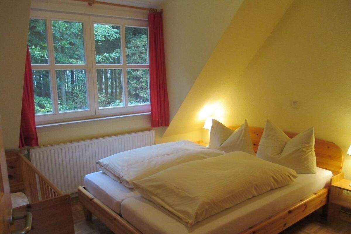 A bedroom with a wooden bed, a window with a view of trees, a radiator, and a bedside table with a lamp.