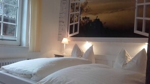A bedroom with two beds, a nightstand, a lamp, and a window with curtains. - Ennenhof (Schneverdingen)