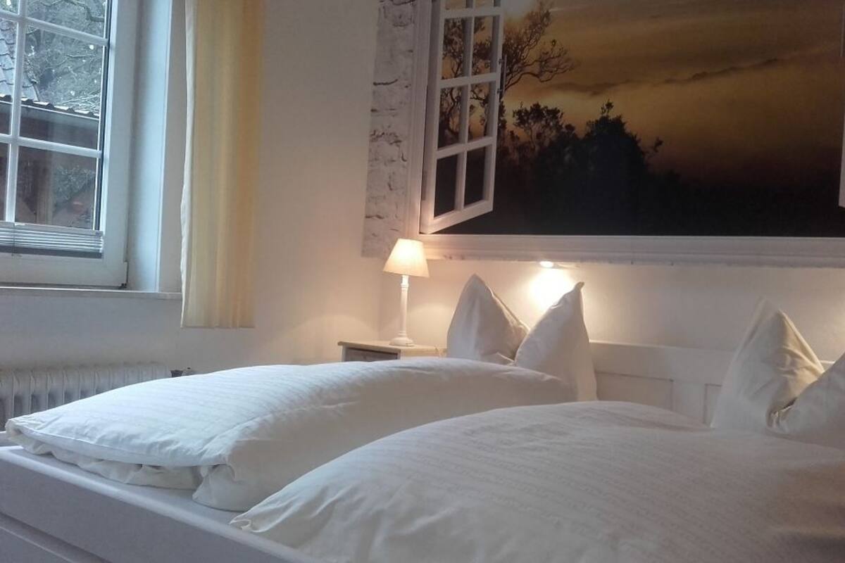 A bedroom with two beds, a nightstand, a lamp, and a window with curtains.
