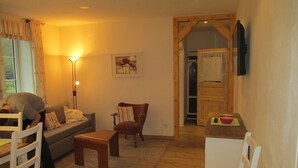 A cozy living room with a sofa, armchair, and wooden coffee table. A lamp provides warm lighting, and a painting adorns the wall. - Ennenhof (Schneverdingen)
