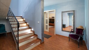 Un escalier avec des marches en bois et des rampes noires, un miroir au mur et une chaise sur laquelle est posé un chapeau.