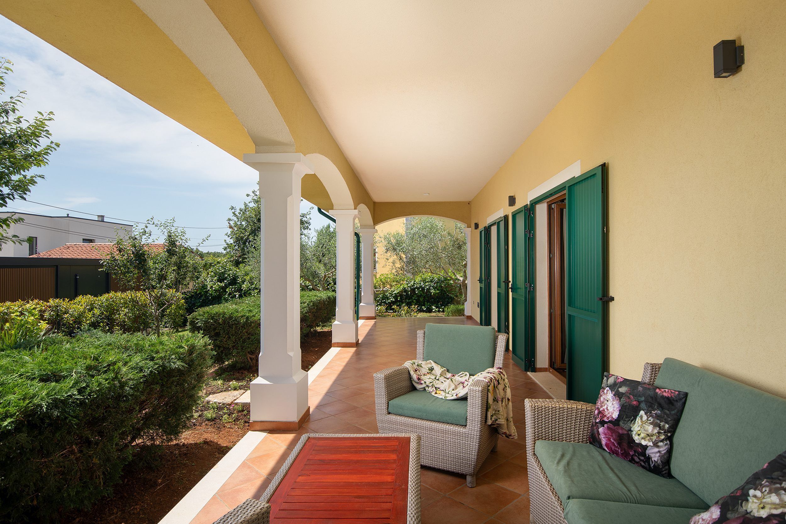 A covered outdoor area with a wicker sofa, a wooden table, and a chair.