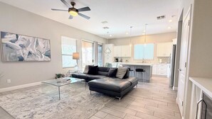 A spacious living room with a black leather sofa, a glass coffee table, and a modern ceiling fan. - Modern Chandler Home - Heated Pool, Golf, Fire Pit (Chandler)