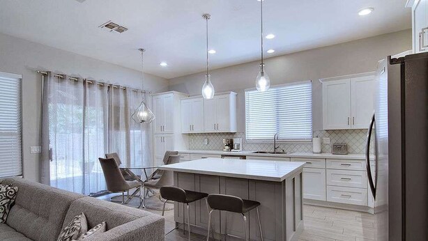 A modern kitchen with white cabinets, a central island with bar stools, pendant lighting, and a refrigerator. - Modern Chandler Home - Heated Pool, Golf, Fire Pit (Chandler)
