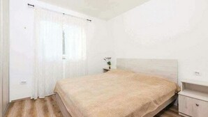 A bedroom with a bed, a nightstand, and a window with curtains. - Apartments Nika (Vinodol)