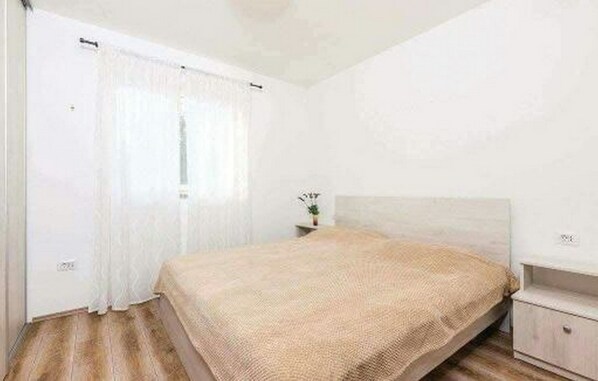 A bedroom with a bed, a nightstand, and a window with curtains.