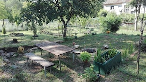 A garden with a wooden table and benches, surrounded by trees and a house in the background. - Apartments Nika (Vinodol)