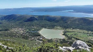 A panoramic view of a coastal landscape with a large body of water, green hills, and a small town with visible buildings. - Apartments Nika (Vinodol)