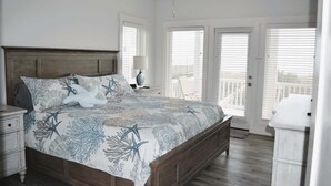 Ein Schlafzimmer mit Bett, Nachttisch, Lampe, Deckenventilator und Blick durch die Tür.