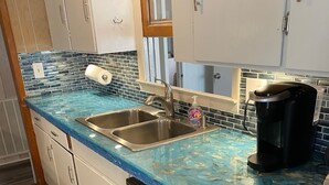 A kitchen with a blue countertop, stainless steel sink, dishwasher, and a coffee maker.