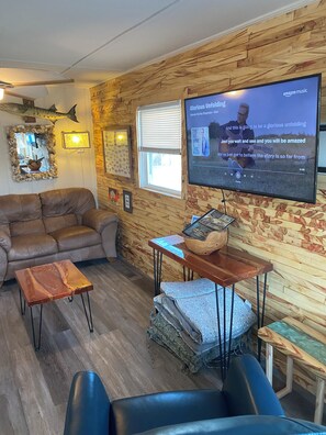A cozy living room with a wooden wall, a large flat-screen TV, a leather sofa, a coffee table, and a patterned rug. - PET FRIENDLY 65 steps to ocean! Directly across the steet from beach access.  (Ocean Isle Beach)
