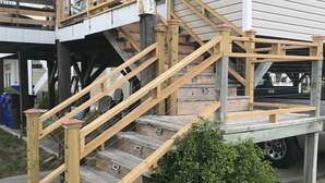 A wooden staircase leading to a covered porch area with a vehicle parked underneath.