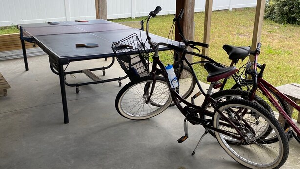 A covered outdoor area with a table and two bicycles parked under a wooden structure.