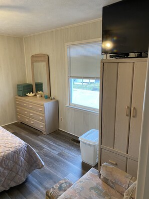 A bedroom with a dresser, a mirror, a television on top, a window with blinds, and a bed. - PET FRIENDLY 65 steps to ocean! Directly across the steet from beach access.  (Ocean Isle Beach)