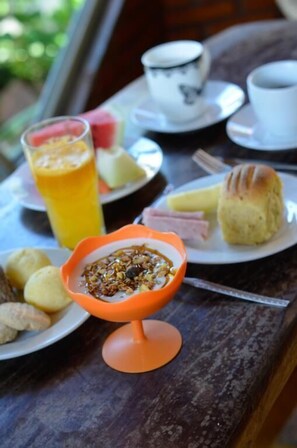 Une table avec des aliments pour le petit-déjeuner, notamment un verre de jus d’orange, un bol de granola, des biscuits et une assiette avec du jambon et un muffin.