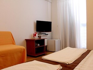 Une chambre d’hôtel avec un lit, une télévision, un petit réfrigérateur, une armoire rouge et une fenêtre avec des rideaux.