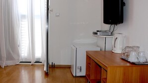 A room with a wooden floor, a white refrigerator, a coffee maker, and a TV mounted on the wall. - Apartmani Krka Rooms (Sibenik)