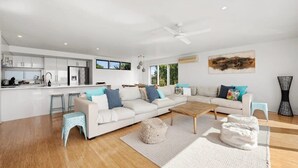 A modern living space with a kitchen, a large sofa set, a coffee table, and a ceiling fan.