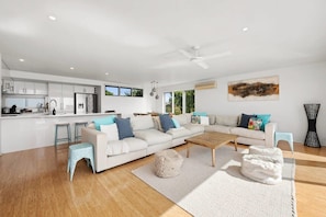 A modern living space with a kitchen, a large sofa set, a coffee table, and a ceiling fan.