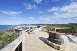 A wooden deck with a stone bench and a satellite dish, overlooking a coastal landscape.