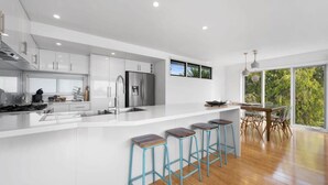A modern kitchen with white cabinetry, a stainless steel refrigerator, and a bar area with stools.
