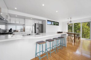 A modern kitchen with white cabinetry, a stainless steel refrigerator, and a bar area with stools.