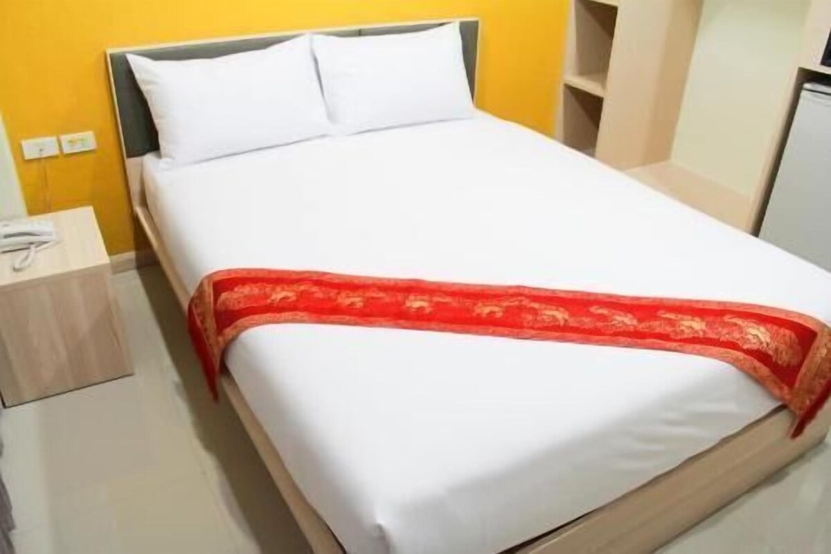 Un lit avec une literie blanche et une couverture rouge, une table de chevet avec un téléphone, et un mur jaune.