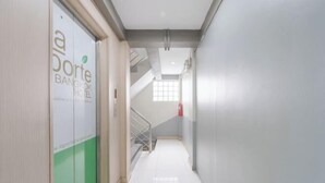 En hotelgang med en trappe der fører op til en etage, en brandslukker på væggen og en dør med et grønt og hvidt design.