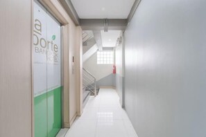 Een hotelgang met een trap die naar een verdieping leidt, een brandblusser aan de muur, en een deur met een groen-wit ontwerp.