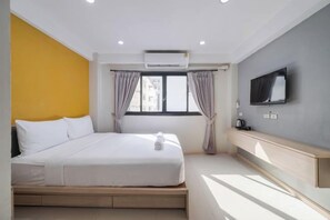 Una habitación de hotel con cama, televisor, ventana con cortinas y aire acondicionado.