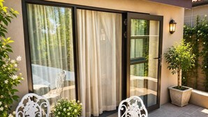 A patio with a table and chairs, a potted plant, and a sliding glass door with curtains. - Moonriver Guesthouse (Upington)