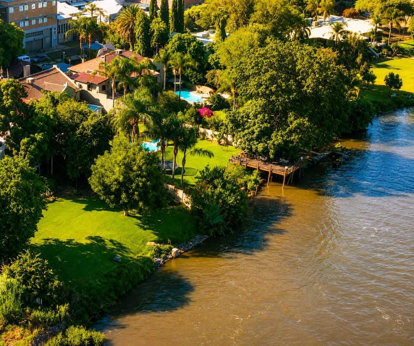 Una propiedad junto al río con piscina, exuberante vegetación y un muelle de madera.