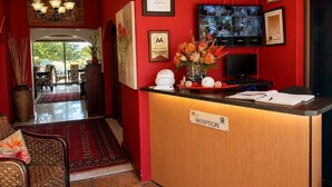 A reception area with a red wall, a reception desk, a television, and various framed certificates and awards. - Moonriver Guesthouse (Upington)