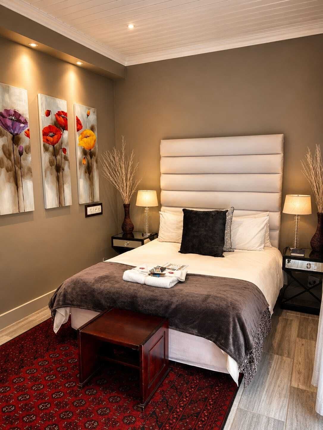 A bedroom with a large bed, two bedside tables, a nightstand, a red patterned rug, and three wall-mounted paintings.