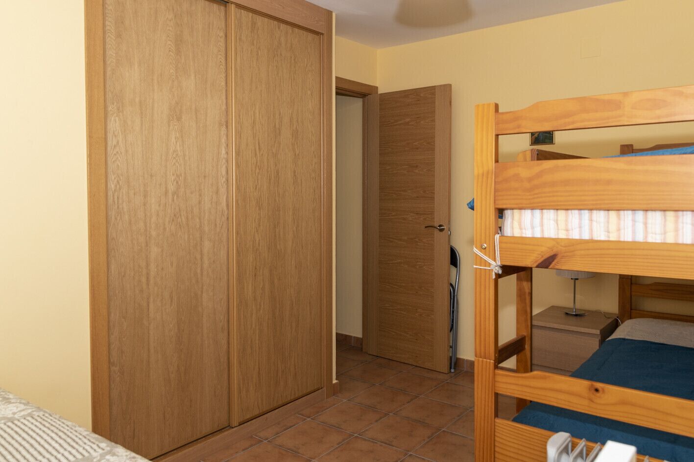 A bedroom with a wooden bunk bed, a wardrobe, and a door leading to another room.