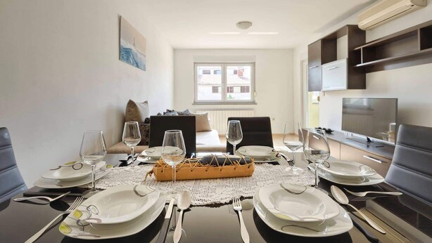 A dining area with a table set for four, including plates, cutlery, and wine glasses. - Apartment Marko (Pula)