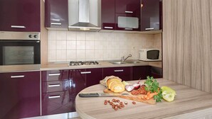 A kitchen with dark cabinets, a microwave, a stove, and a cutting board with vegetables and nuts. - Apartment Marko (Pula)