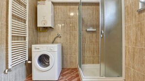 A bathroom with a glass-enclosed shower, a built-in washing machine, and a wall-mounted heater. - Apartment Marko (Pula)