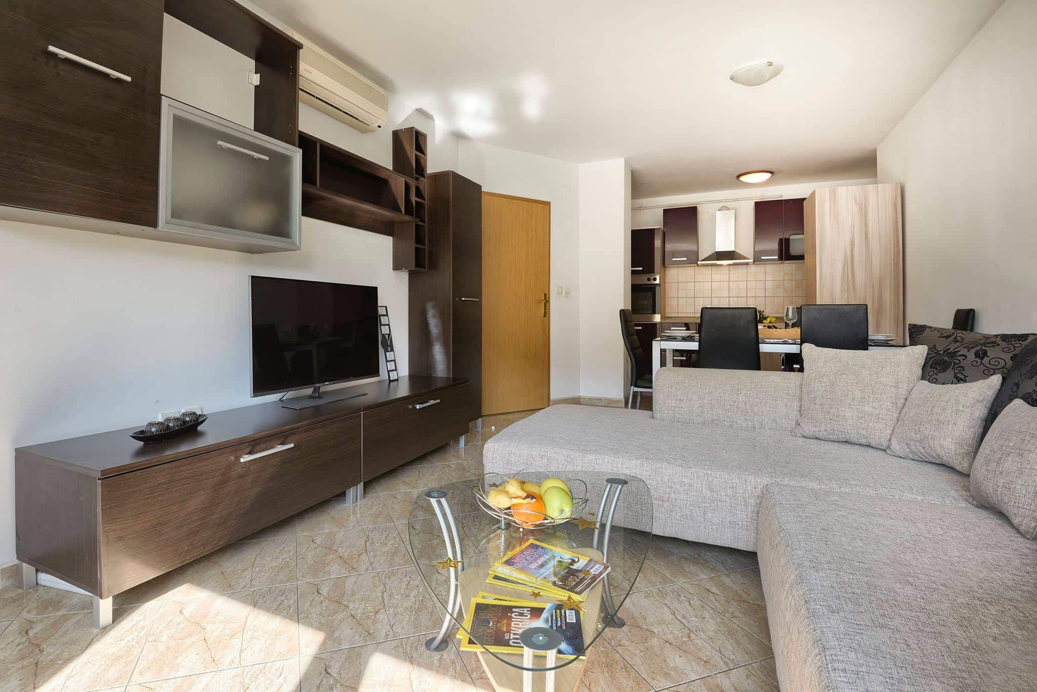 A modern living room with a sofa, TV, and a glass coffee table with magazines.