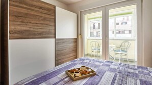 A bedroom with a bed, a wooden wardrobe, and a balcony with chairs. - Apartment Marko (Pula)