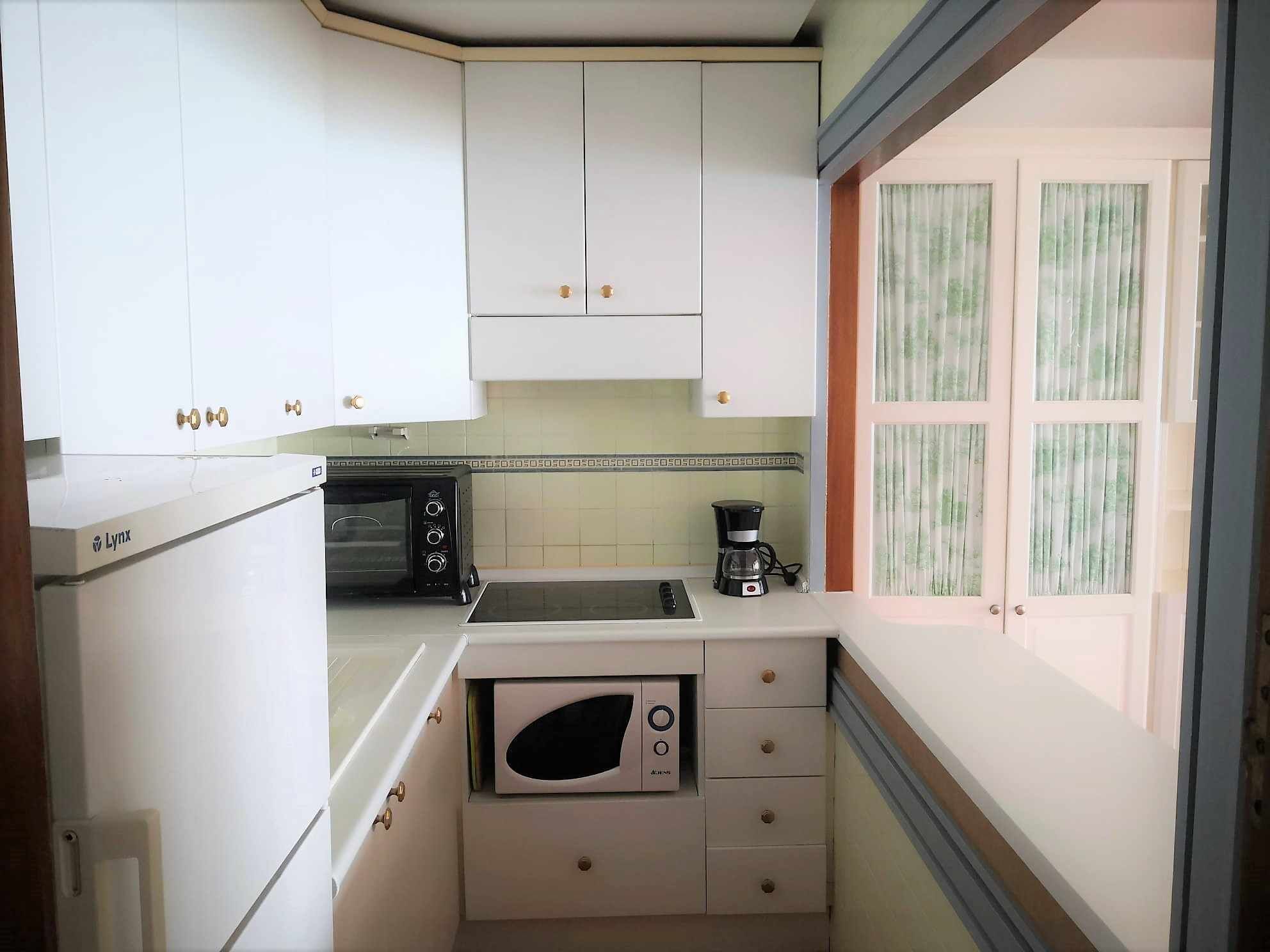 A compact kitchen with white cabinets, a built-in microwave, a coffee maker, and a toaster.