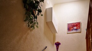 Una escalera con barandilla, un pequeño estante de madera con un jarrón y un cuadro en la pared.