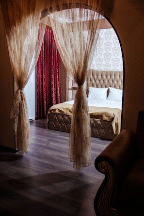 A bedroom with a tufted headboard, a bed with white linens, and a large window with red curtains. - Bagchali Hotel (Shabran)