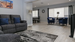 A living room with a grey sofa, blue armchairs, a dining table, and a large window with blinds. - Home away from home! (South Pasadena)